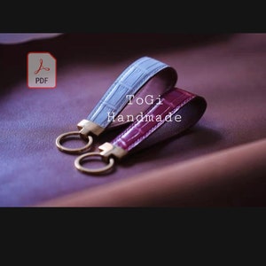 May include: Two leather keychains with gold key rings. One keychain is light blue and the other is burgundy. The keychains have a crocodile pattern and the text "ToGi Handmade" is printed on the burgundy keychain.