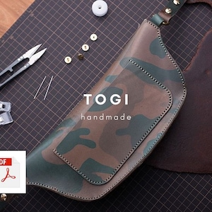 May include: A camouflage-patterned leather fanny pack with a brown leather strap and a metal buckle. The bag has a small pocket on the front and the text "TOGI handmade" is printed on the front. The bag is lying on a black and white gridded surface.