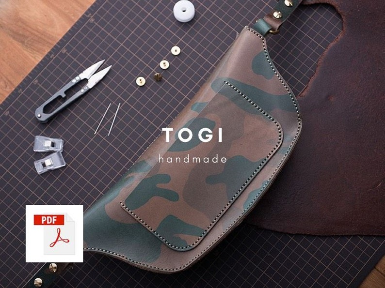 May include: A camouflage-patterned leather fanny pack with a brown leather strap and a metal buckle. The bag has a small pocket on the front and the text "TOGI handmade" is printed on the front. The bag is lying on a black and white gridded surface.