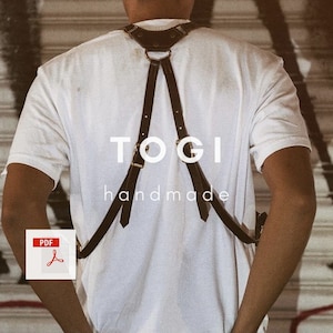 May include: A person wearing a white t-shirt with a black leather harness. The harness has a gold ring and the text "TOGI handmade" is printed on the front.