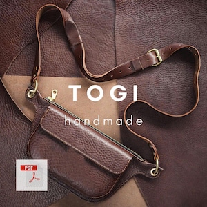 Może przedstawiać: Brązowa skórzana torba na ramię z regulowanym paskiem i złotymi okuciami. Torba posiada zapinaną na zamek komorę główną i przednią klapę. Na torbie wydrukowano słowa "TOGI" i "handmade".
