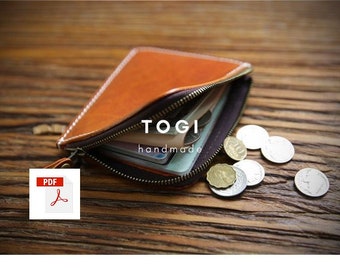 May include: A brown leather wallet with a zipper closure and the text "TOGI handmade" on the front. The wallet is open and has several cards and bills inside. There are also several coins scattered on a wooden surface.