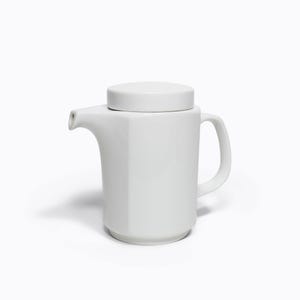 May include: A white ceramic teapot with a lid. The teapot has a cylindrical body with a handle and a spout. The lid is flat and round. The teapot is designed with a modern aesthetic and is suitable for serving tea or other hot beverages.