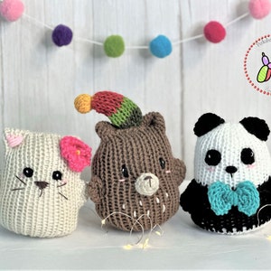 May include: Three crocheted stuffed toys: a white cat with a pink flower, a brown bear wearing a colourful hat, and a black and white panda with a blue bow tie.