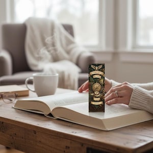 Może przedstawiać: Ozdobna zakładka do książki z napisem "Knowledge is the Key" i wzorem kompasu. Zakładka znajduje się w otwartej książce na drewnianym stole, z filiżanką kawy i okularami w pobliżu. Scena rozgrywa się w przytulnym salonie.