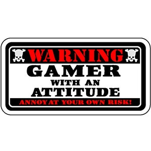 May include: A rectangular sign with a black border and white background. The top of the sign reads "WARNING" in red, with a skull and crossbones on each side. Below, in large black letters, it says "GAMER WITH AN ATTITUDE". The bottom reads "ANNOY AT YOUR OWN RISK!" in red.