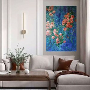 May include: A rectangular wall art piece featuring an oil painting of vibrant coral-pink roses blooming on leafy green stems against a deep, textured blue background with vertical brushstrokes, displayed on a light gray wall above a sofa.