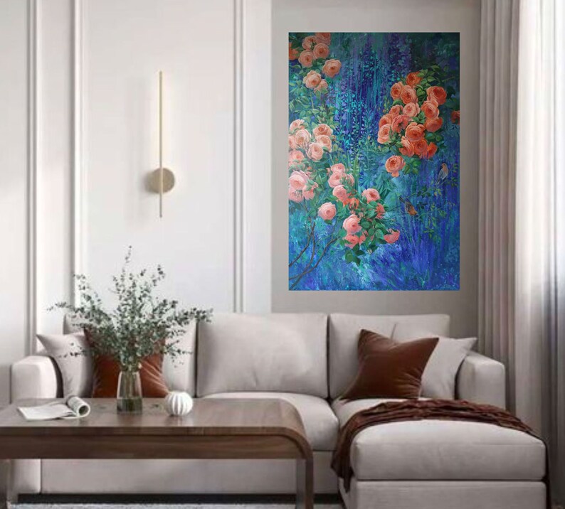 May include: A rectangular wall art piece featuring an oil painting of vibrant coral-pink roses blooming on leafy green stems against a deep, textured blue background with vertical brushstrokes, displayed on a light gray wall above a sofa.