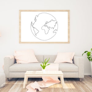 May include: A framed print of a line drawing of the Earth hangs above a gray sofa with pink pillows. A small wooden table with a pink throw and a potted plant are in front of the sofa. A floor lamp and a potted plant are also in the room.