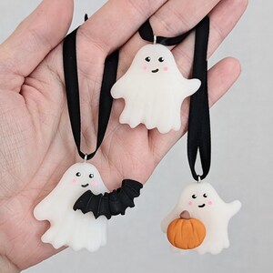 May include: Three white ghost ornaments with black ribbon. One ghost has a black bat, one has a small orange pumpkin, and one has a simple smiling face.