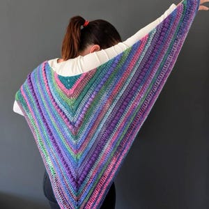 Pu&ograve; includere: Uno scialle all'uncinetto fatto a mano, di forma triangolare e multicolore. Lo scialle presenta una vivace miscela di colori, tra cui viola, blu, verde e rosa, disposti a righe. La trama sembra avere un punto in rilievo, tipo a pallini.