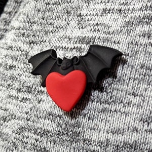 May include: A black bat with a red heart in the centre. The bat is made of rubber and has a glossy finish.