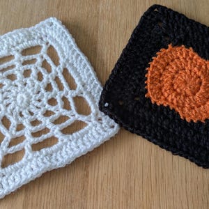 May include: Two square crochet motifs. One motif is white with an openwork spiderweb pattern. The second motif is black with a solid orange circular center. Both pieces are crafted from yarn and feature a square shape with distinct stitch textures.