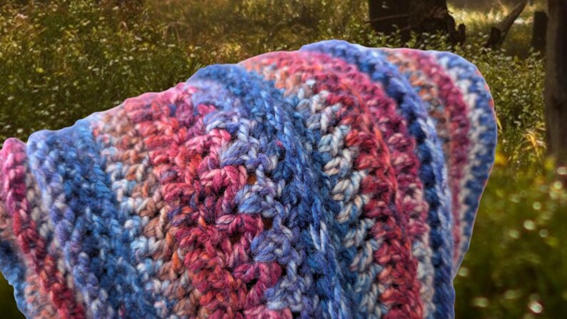May include: A crocheted blanket with stripes of pink, blue, and white yarn. The blanket is folded in half and has a soft, textured look.