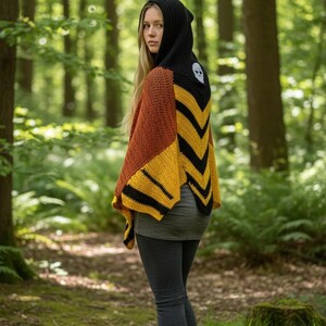 May include: A hooded crochet shawl in shades of brown, yellow, and black, with a skull design on the hood. The shawl is worn over a gray top and dark gray leggings. The background is a forest with green trees.