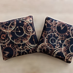 May include: Two square throw pillows with a black background and a gold and brown clock face pattern.