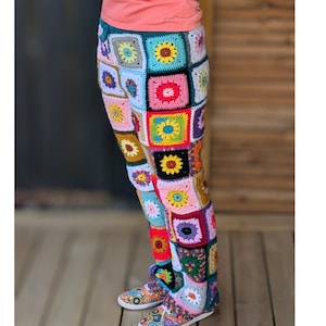 Puede incluir: Pantalones de crochet coloridos con un diseño de patchwork de cuadrados en varios colores, incluyendo rosa, azul, amarillo y verde. Los pantalones tienen una cintura con cordón y se combinan con zapatillas de crochet a juego, creando un atuendo vibrante y llamativo.