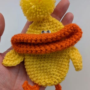 May include: A handmade yellow crochet duck with an orange beak and feet. The duck has a yellow pom-pom on its head and googly eyes. This whimsical item is a charming addition to any collection.