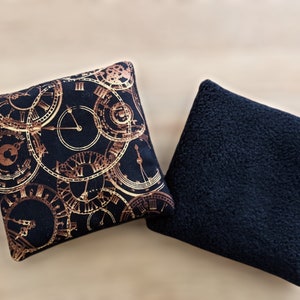 May include: Two square throw pillows. One pillow has a black background with a gold clock pattern. The other pillow is solid black.