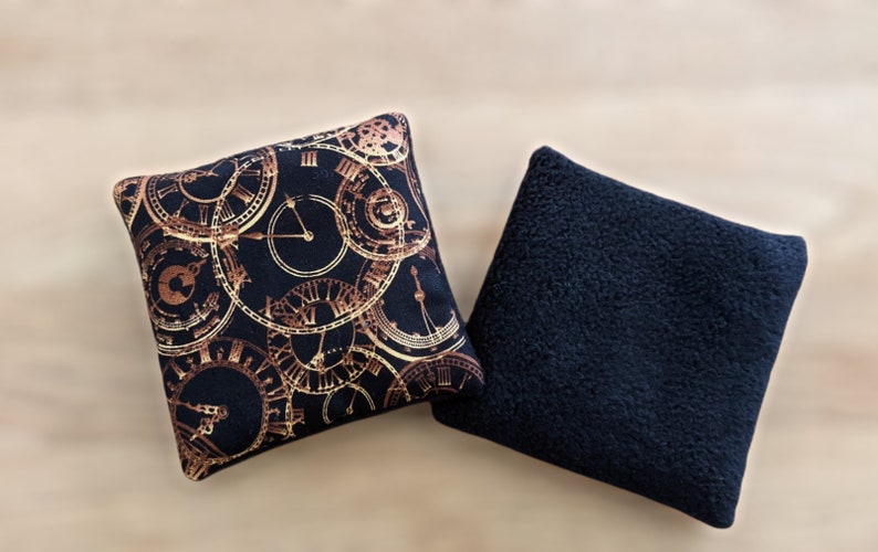 May include: Two square throw pillows. One pillow has a black background with a gold clock pattern. The other pillow is solid black.