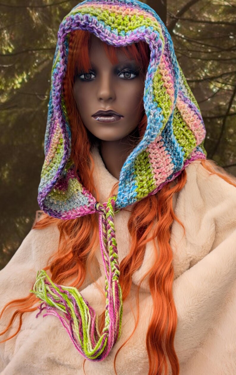May include: A colourful crocheted hooded scarf with a long braided tassel. The scarf is made with a variety of colours, including pink, blue, green, and purple.