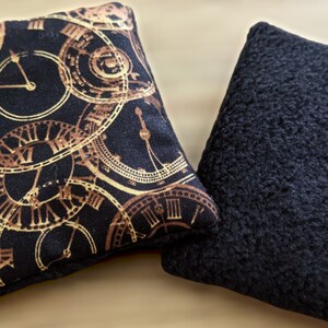May include: Two square-shaped pillows. One pillow has a black background with a gold clock pattern. The other pillow is solid black.