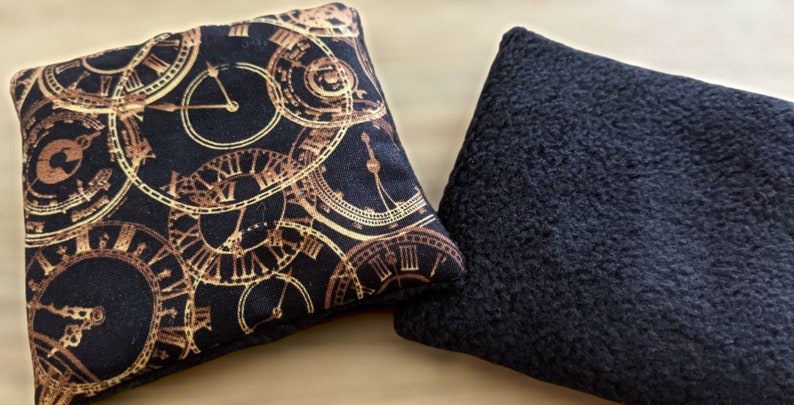 May include: Two square-shaped pillows. One pillow has a black background with a gold clock pattern. The other pillow is solid black.