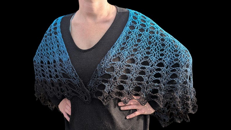 May include: A blue and black crocheted shawl with a gradient effect. The shawl is draped over the shoulders, showcasing an open, lacy design. The color transitions from a bright blue to a deep black.