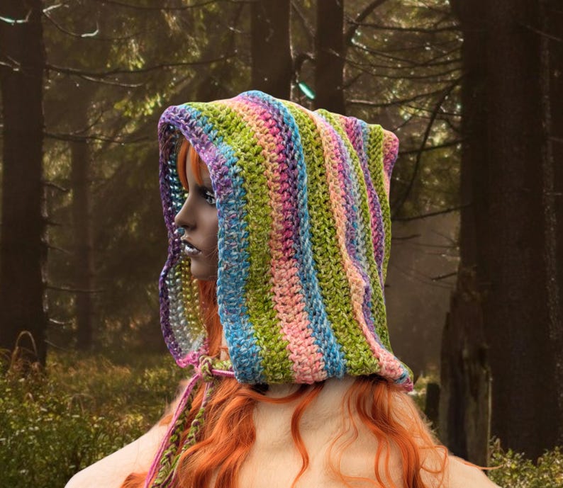 May include: A colourful striped crochet hooded scarf in shades of green, pink, blue, and purple. The scarf is worn by a person with long red hair.
