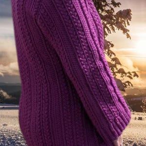 May include: A long-sleeved, purple knitted sweater with a textured cable knit pattern. The sweater has a high neckline and a fitted silhouette. The background features a winter landscape with snow and a sunset.