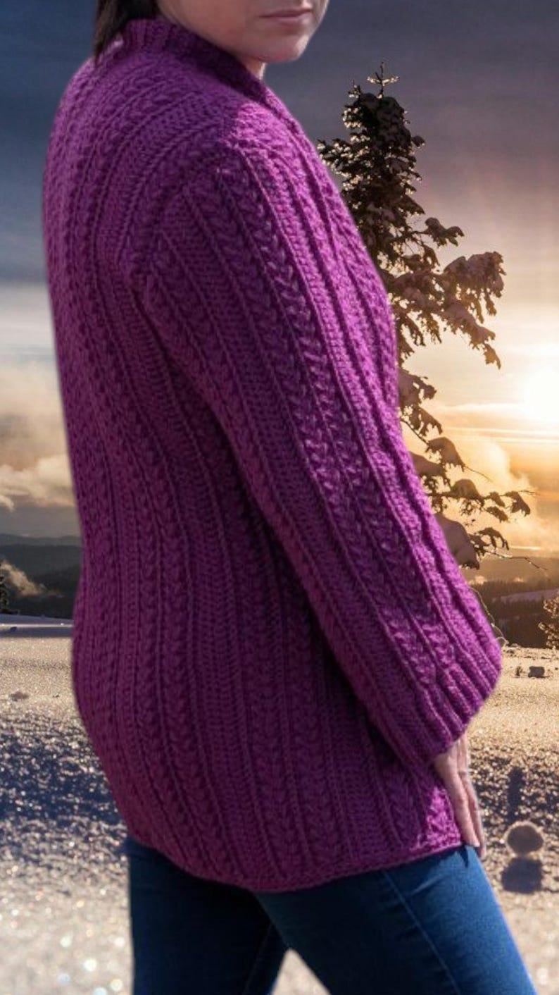 May include: A long-sleeved, purple knitted sweater with a textured cable knit pattern. The sweater has a high neckline and a fitted silhouette. The background features a winter landscape with snow and a sunset.