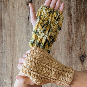 May include: Two handmade crochet fingerless gloves. One glove is a mix of yellow, green, and cream colors. The other glove is a solid tan color. Both gloves have a textured, braided design.