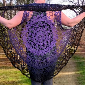 May include: A handmade, open-weave crochet shawl in a circular design. The shawl features a gradient of colors, transitioning from a deep purple center to black edges. The intricate pattern is visible throughout the garment.