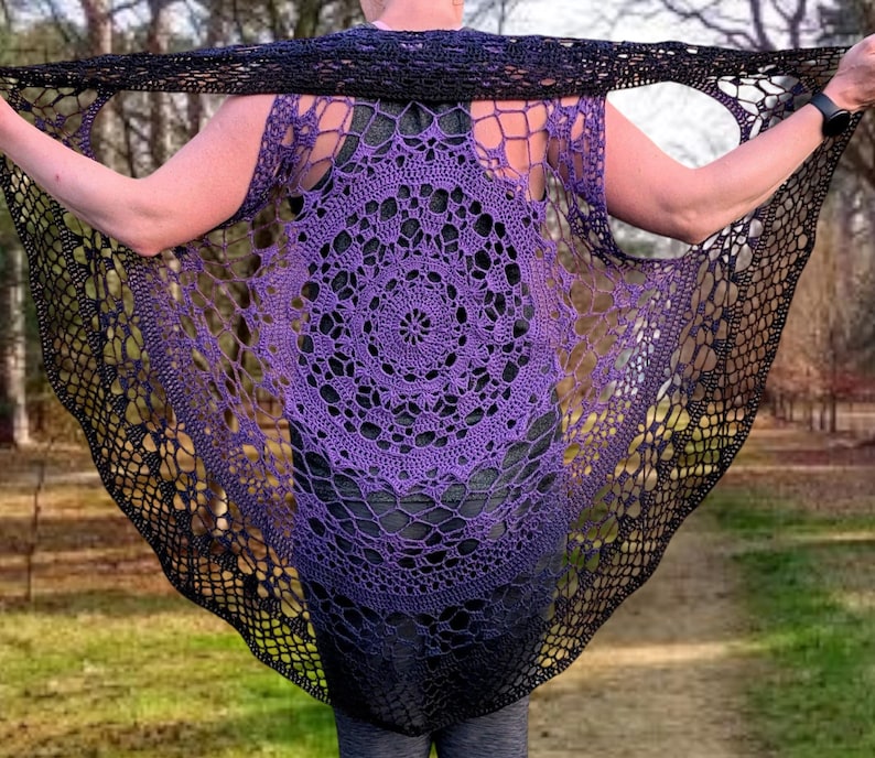May include: A handmade, open-weave crochet shawl in a circular design. The shawl features a gradient of colours, transitioning from a deep purple centre to black edges. The intricate pattern is visible throughout the garment.