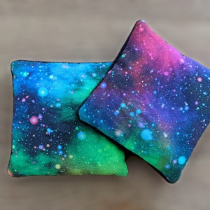May include: Two square throw pillows with a galaxy print. The pillows are black with a blue, green, and pink nebula design.