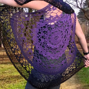 May include: A handmade crochet shawl in shades of purple and black. The openwork design features a circular pattern in the centre, with a gradient effect from purple to black. The shawl is draped over the shoulders.