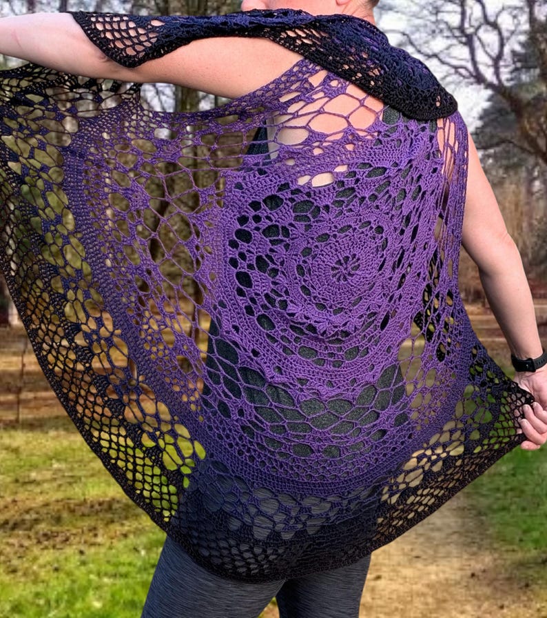 May include: A handmade crochet shawl in shades of purple and black. The openwork design features a circular pattern in the centre, with a gradient effect from purple to black. The shawl is draped over the shoulders.
