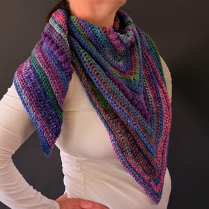 Pu&ograve; includere: Uno scialle all'uncinetto fatto a mano e colorato, nei toni del blu, viola, verde e rosa. Lo scialle triangolare &egrave; drappeggiato intorno al collo, mostrando un motivo a punto strutturato. Il filato sembra essere una miscela di pi&ugrave; colori, creando un effetto a righe.