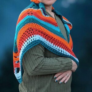 Puede incluir: Un chal de ganchillo hecho a mano en tonos naranja, turquesa y blanco. El chal est&aacute; drapeado sobre los hombros, mostrando el intrincado dise&ntilde;o calado. La combinaci&oacute;n de colores crea un accesorio vibrante y llamativo.
