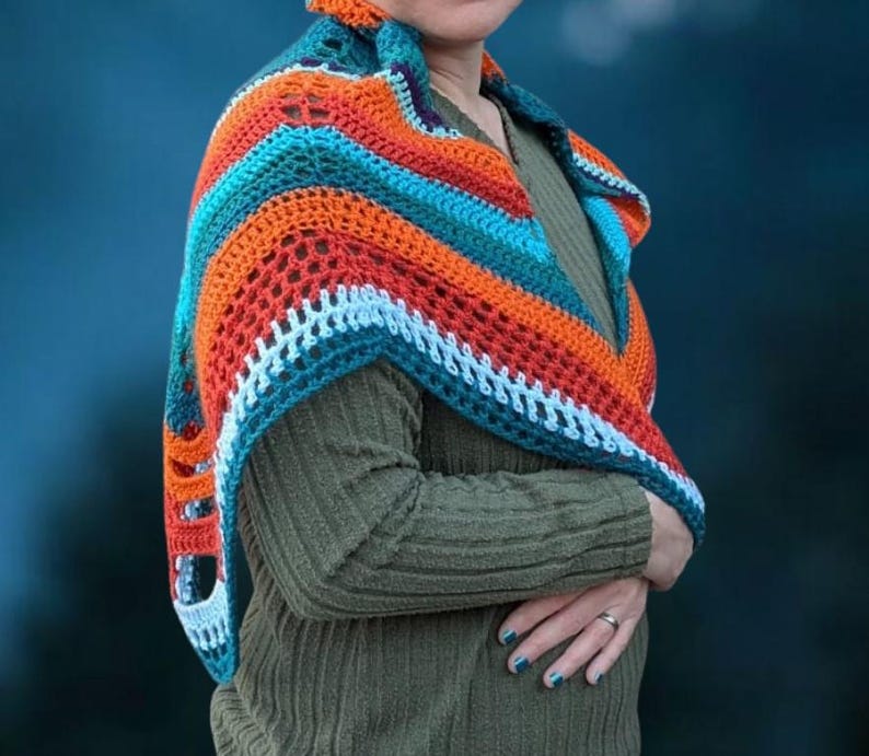 Puede incluir: Un chal de ganchillo hecho a mano en tonos naranja, turquesa y blanco. El chal est&aacute; drapeado sobre los hombros, mostrando el intrincado dise&ntilde;o calado. La combinaci&oacute;n de colores crea un accesorio vibrante y llamativo.