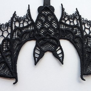 May include: Black lace bat applique with intricate details. The bat is hanging from a string and has a delicate, intricate design.