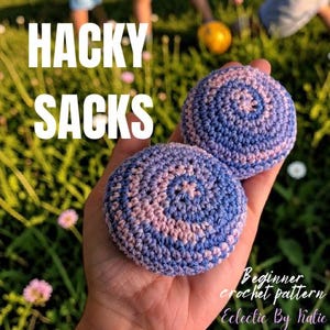 Puede incluir: Dos pelotas de malabares tejidas a ganchillo con un patrón en espiral en hilo azul y violeta claro. El texto HACKY SACKS aparece en blanco en la parte superior, con Beginner crochet pattern Eclectic By Katie en blanco abajo a la derecha.