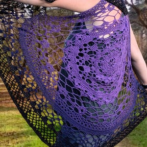 May include: A handmade crochet shawl in a gradient of purple to black. The openwork design features a spiral pattern and a delicate, lacy texture. The shawl is draped over the shoulders, showcasing the intricate craftsmanship and colour transition.