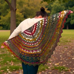 May include: A multi-coloured, open-weave shawl in shades of green, red, yellow, and purple. The shawl is draped over the shoulders, showing its intricate crochet design. The edges have a scalloped trim. A handmade accessory.