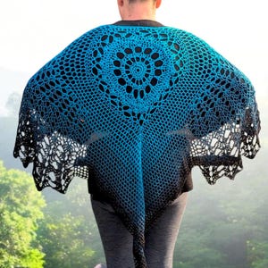 May include: A blue and black crocheted shawl with a circular design in the center. The shawl has a gradient effect, transitioning from blue to black. The open weave design is visible, and the shawl is worn outdoors.