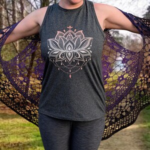 May include: A dark grey vest top featuring a white and pink lotus flower design. A black and purple crocheted shawl is draped over the shoulders. The shawl has an openwork pattern.