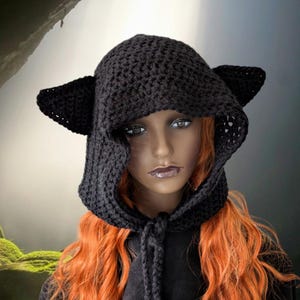 Puede incluir: Sombrero de punto negro con capucha y orejas de gato. El sombrero est&aacute; hecho de un hilo suave y c&aacute;lido y tiene una capucha larga y fluida. Las orejas est&aacute;n unidas a la parte superior de la capucha y tienen unos 7,5 cm de largo.