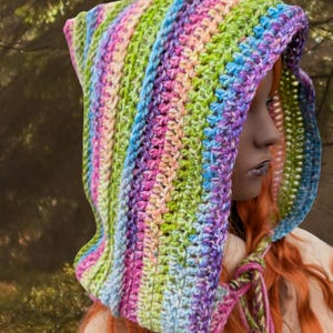 May include: A colourful crocheted hooded scarf with a rainbow stripe pattern. The scarf is tied with a long, thin cord.