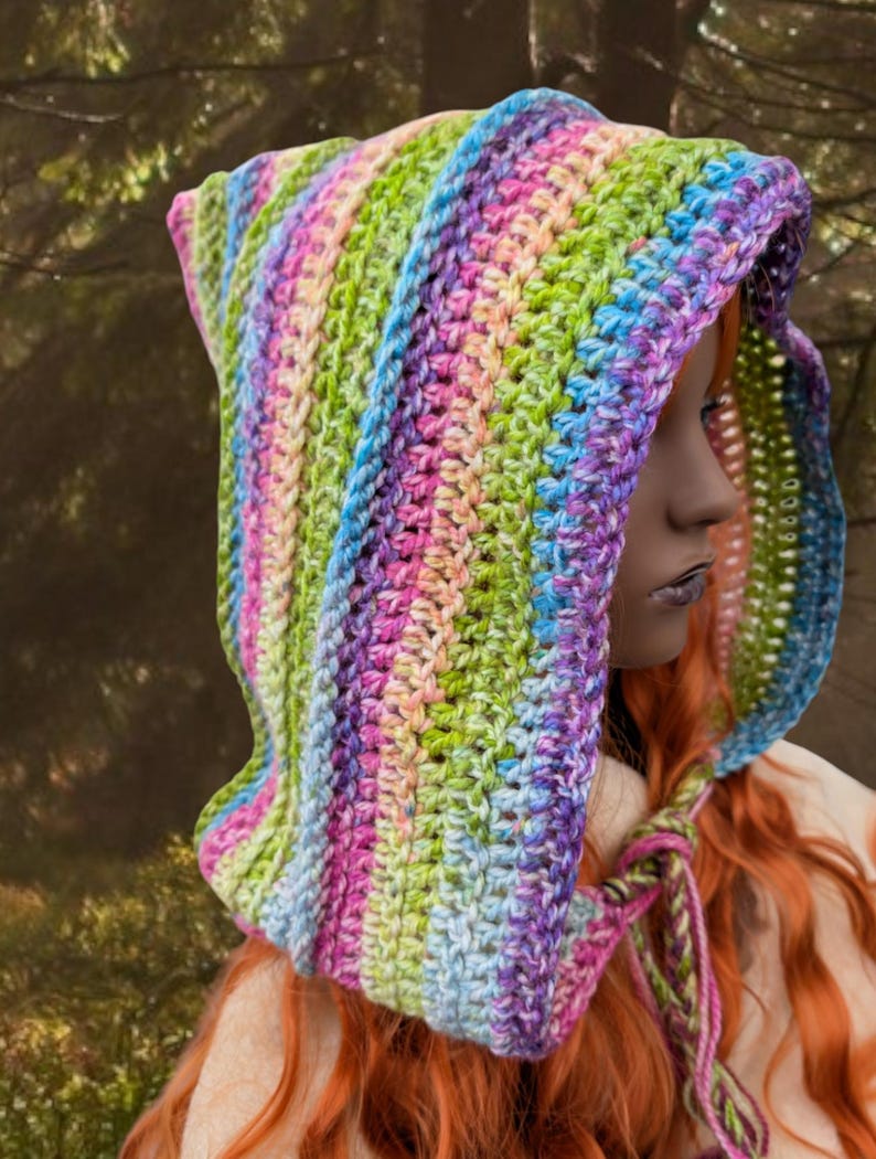 May include: A colourful crocheted hooded scarf with a rainbow stripe pattern. The scarf is tied with a long, thin cord.