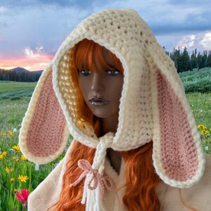 May include: A white crocheted hooded scarf with pink bunny ears. The scarf has a long tie that can be tied in a bow.